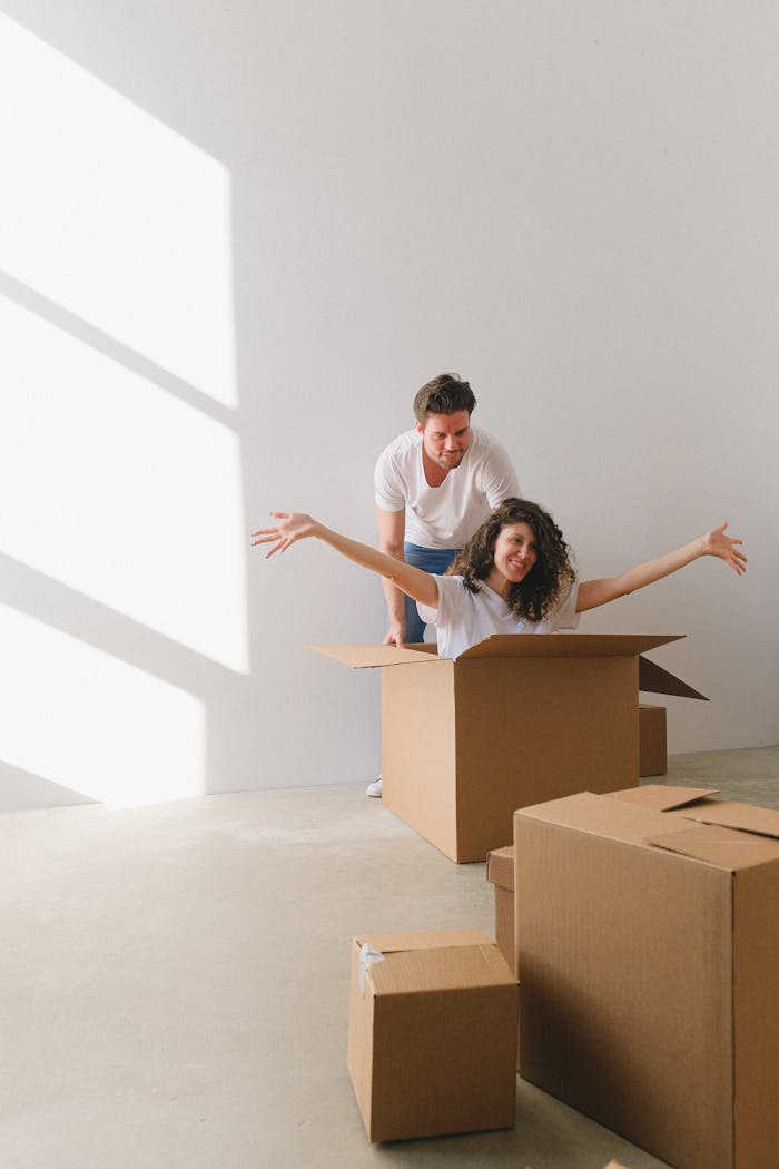 A joyful couple having fun with cardboard boxes in a bright, sunny room, symbolizing moving and new beginnings.